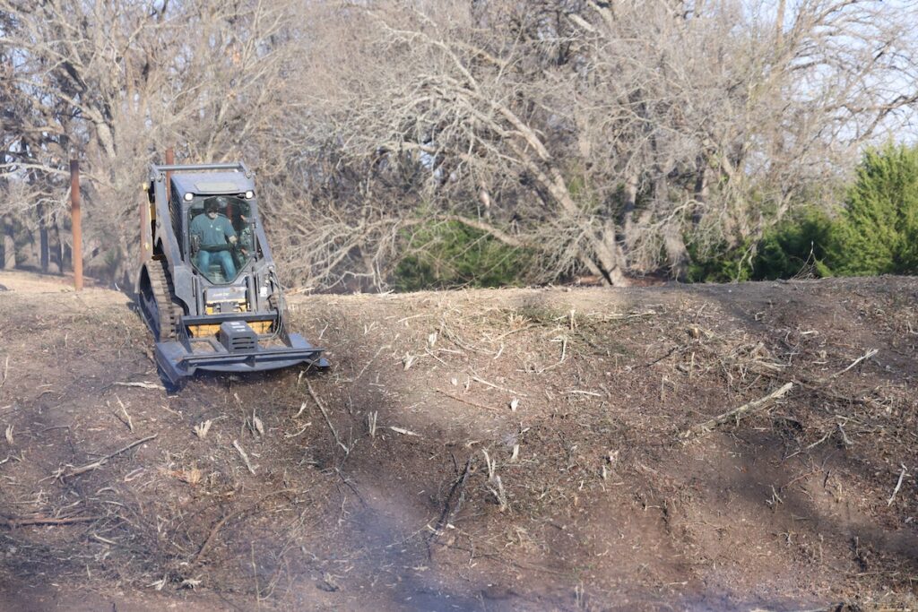 Man in plaid shirt using chainsaw to cut tree branches outdoors.