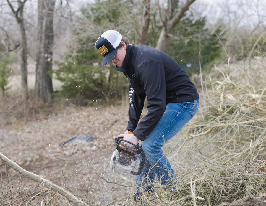 Man cutting tree branches outdoors with a chainsaw.